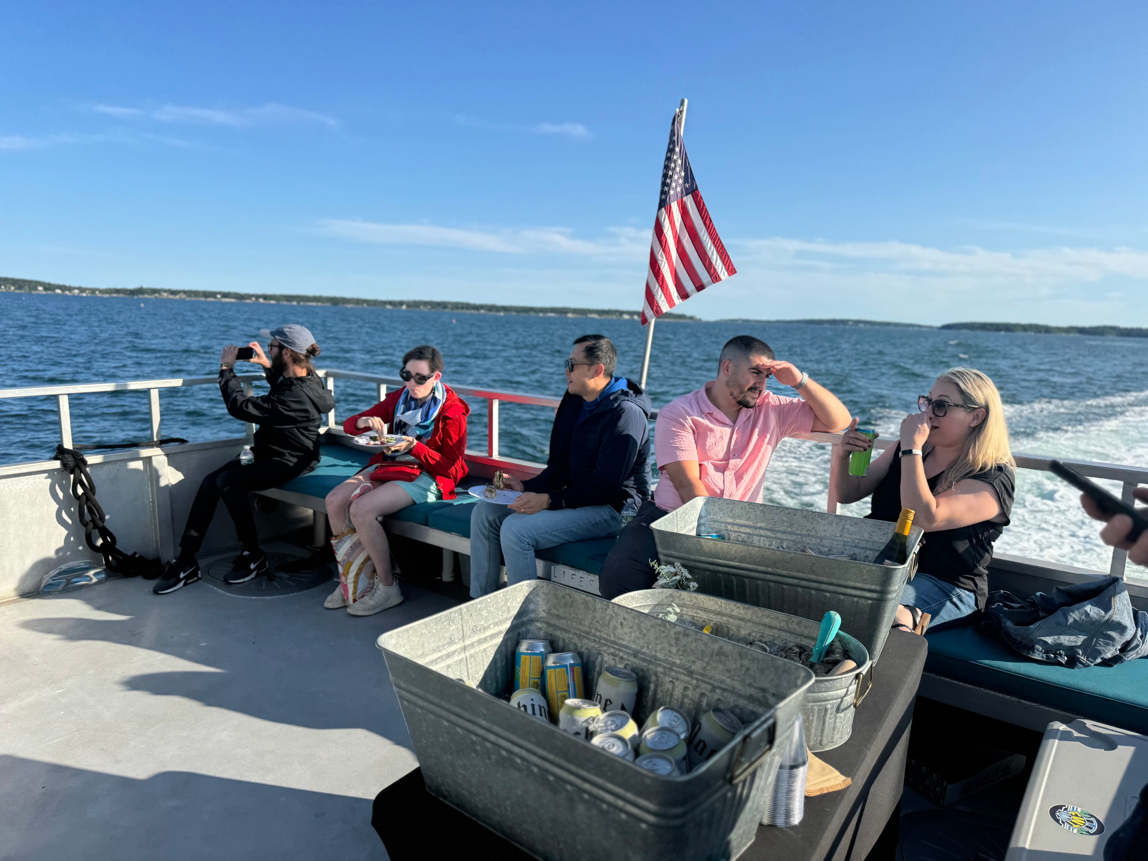 Group of people on a boat with an American flag, enjoying a sunny day on the water.